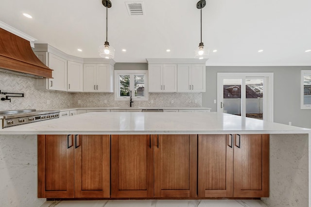 kitchen featuring a center island, custom range hood, decorative light fixtures, light stone counters, and white cabinetry