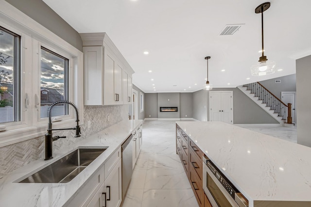 kitchen with tasteful backsplash, stainless steel appliances, sink, white cabinetry, and hanging light fixtures