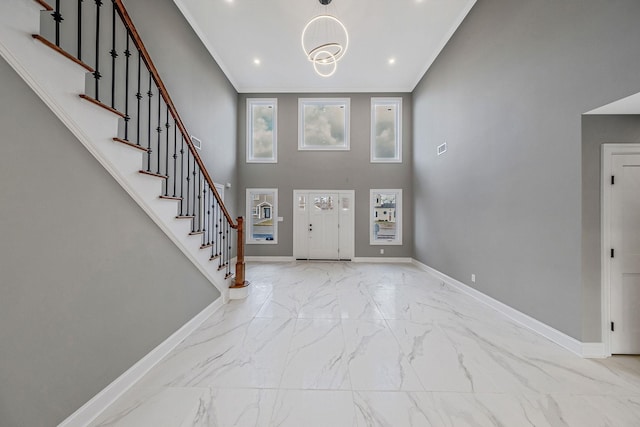 foyer entrance featuring ornamental molding, a towering ceiling, and a notable chandelier