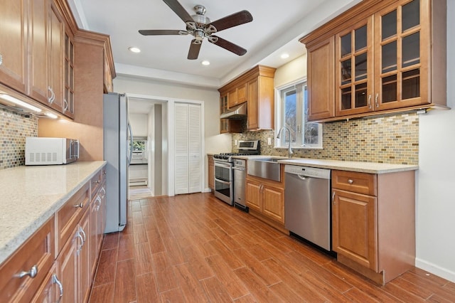 kitchen with under cabinet range hood, brown cabinets, dark wood-style floors, stainless steel appliances, and a sink