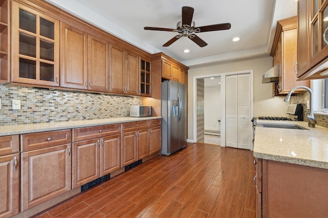 kitchen with stainless steel appliances, dark wood-type flooring, glass insert cabinets, under cabinet range hood, and brown cabinets