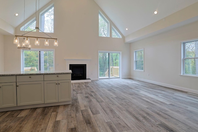 unfurnished living room featuring light hardwood / wood-style flooring, high vaulted ceiling, a wealth of natural light, and a notable chandelier