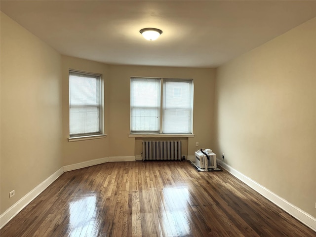 spare room featuring radiator, baseboards, and dark wood-type flooring