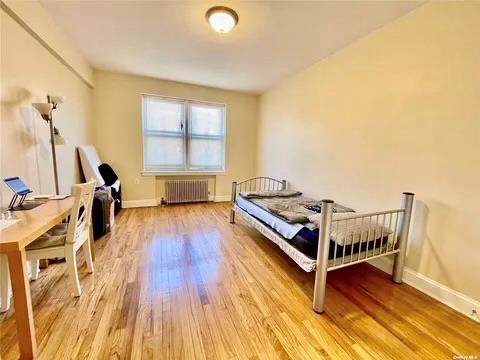 bedroom with light wood finished floors, radiator heating unit, and baseboards