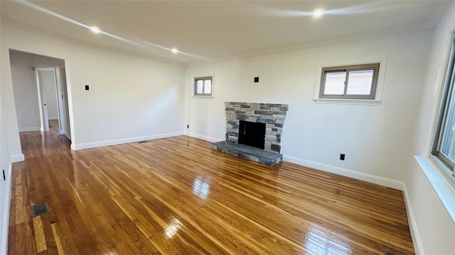 unfurnished living room featuring hardwood / wood-style floors, a stone fireplace, and plenty of natural light