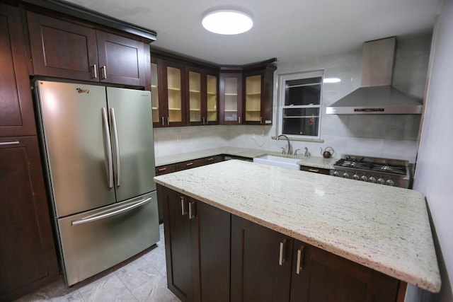 kitchen featuring a center island, wall chimney range hood, sink, light stone countertops, and appliances with stainless steel finishes