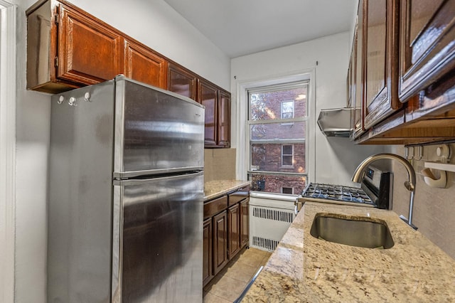 kitchen with stainless steel fridge, radiator heating unit, light tile patterned flooring, light stone countertops, and sink