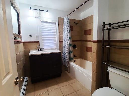 full bathroom with a baseboard radiator, tile patterned floors, tile walls, toilet, and shower / bath combo