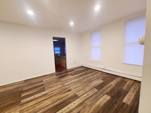 unfurnished room with a baseboard heating unit and dark hardwood / wood-style flooring