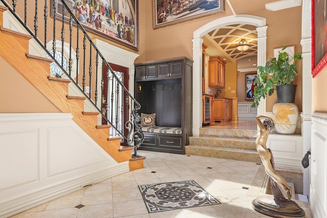 entrance foyer featuring sink, light tile patterned floors, beam ceiling, beverage cooler, and decorative columns