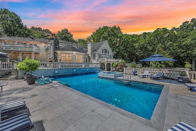 pool at dusk with a patio area and an in ground hot tub