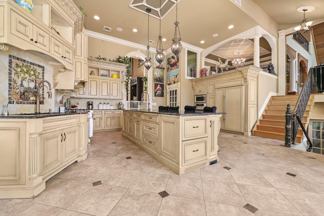 kitchen featuring pendant lighting, cream cabinets, sink, decorative backsplash, and an island with sink