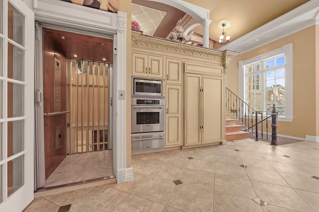 kitchen with elevator, light tile patterned floors, appliances with stainless steel finishes, and cream cabinets