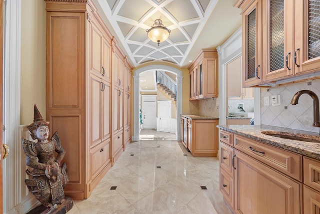 kitchen featuring backsplash, light stone counters, sink, and coffered ceiling