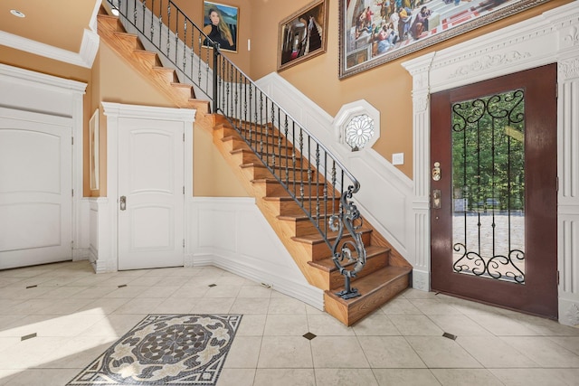 foyer with ornamental molding, light tile patterned floors, and a towering ceiling