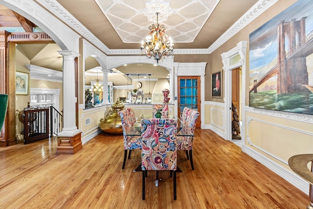 dining area featuring light wood-type flooring, ornate columns, crown molding, and a chandelier