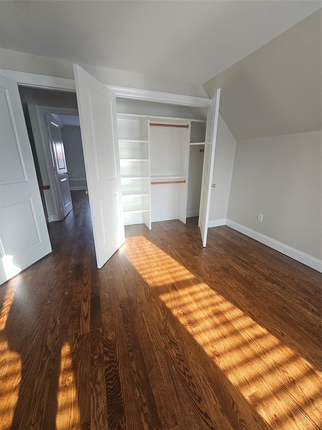 unfurnished bedroom with dark hardwood / wood-style flooring, lofted ceiling, and a closet