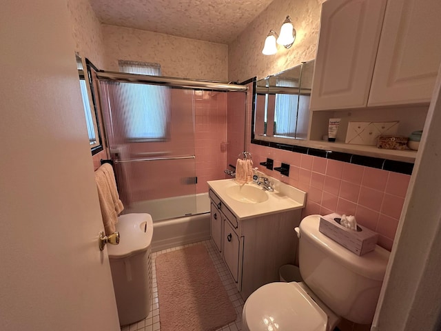 full bathroom featuring tile patterned flooring, combined bath / shower with glass door, toilet, vanity, and tile walls