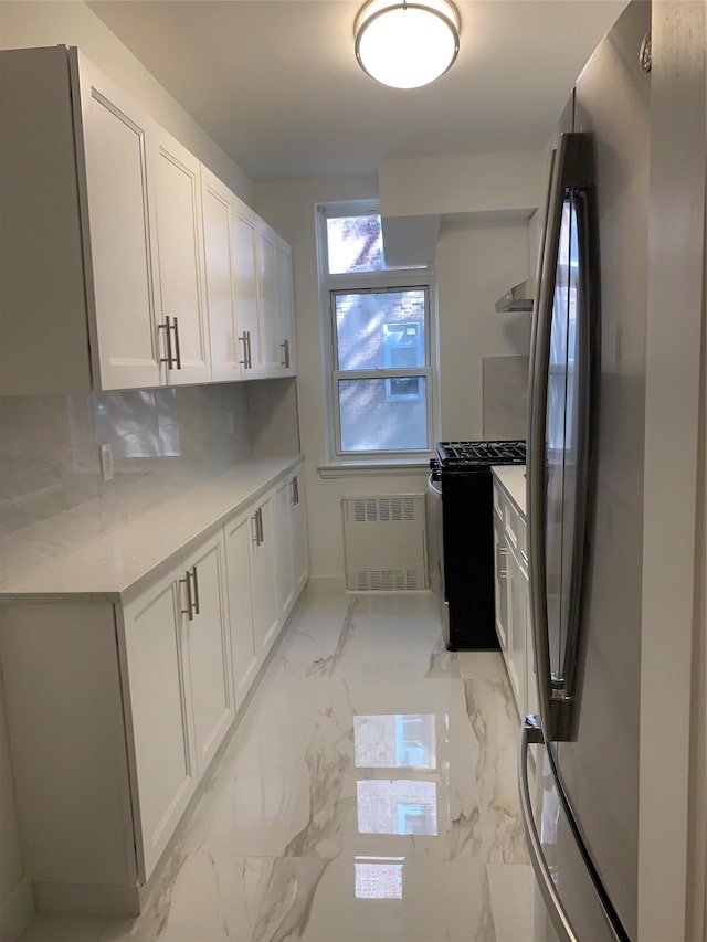 kitchen with light stone countertops, radiator, gas stove, white cabinets, and stainless steel refrigerator