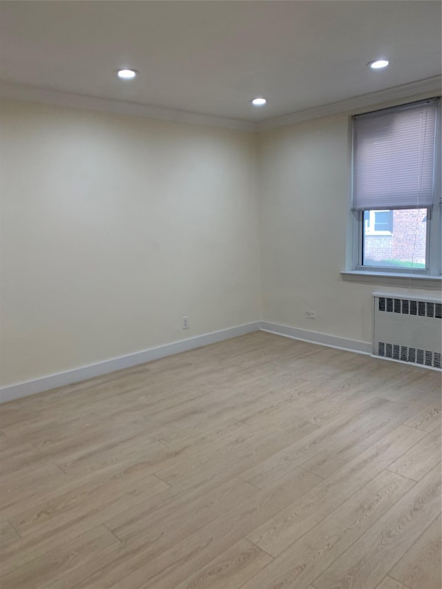 empty room featuring ornamental molding, radiator, and light hardwood / wood-style flooring