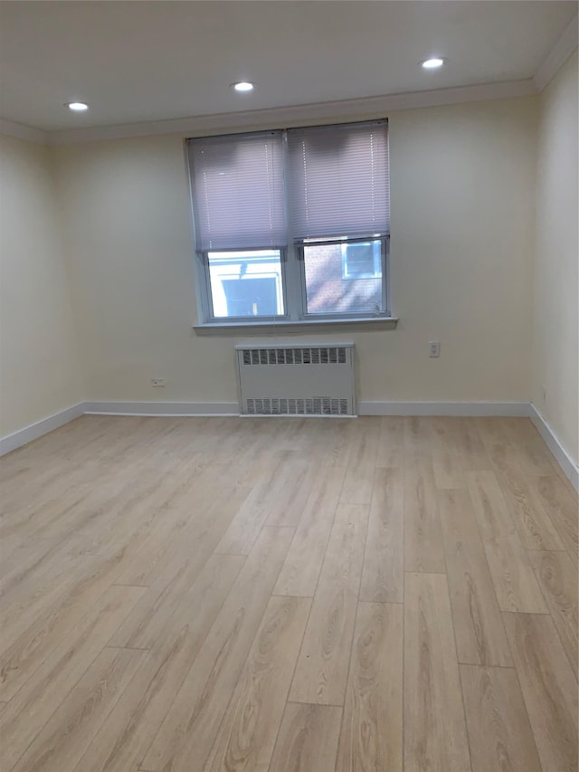 spare room with radiator, ornamental molding, and light wood-type flooring