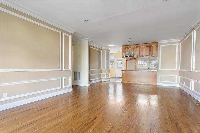 unfurnished living room featuring crown molding, an inviting chandelier, and light wood-type flooring