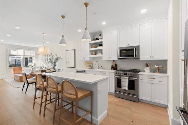 kitchen with white cabinets, pendant lighting, stainless steel appliances, and light hardwood / wood-style floors