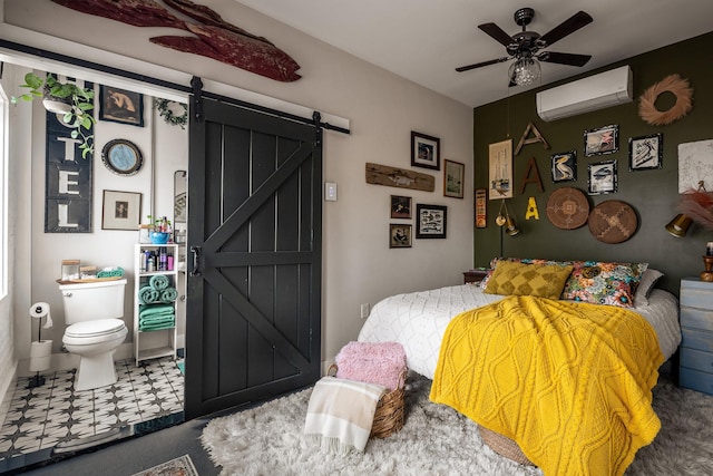 bedroom with ceiling fan, a barn door, an AC wall unit, and connected bathroom