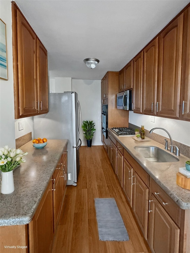 kitchen with light stone countertops, light hardwood / wood-style floors, stainless steel appliances, and sink