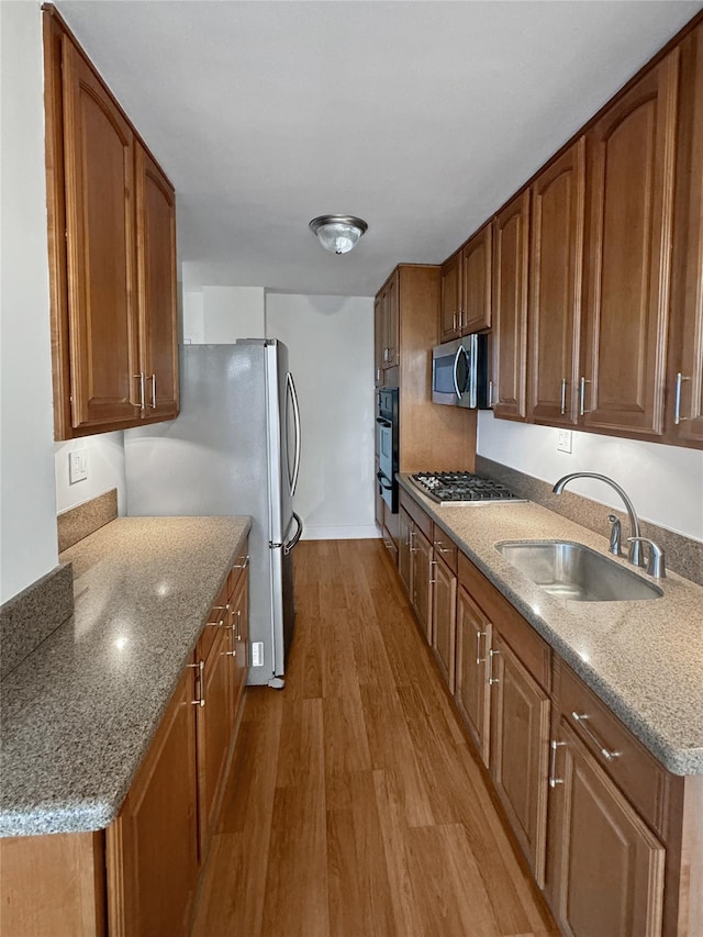 kitchen featuring light stone countertops, stainless steel appliances, sink, and light hardwood / wood-style flooring