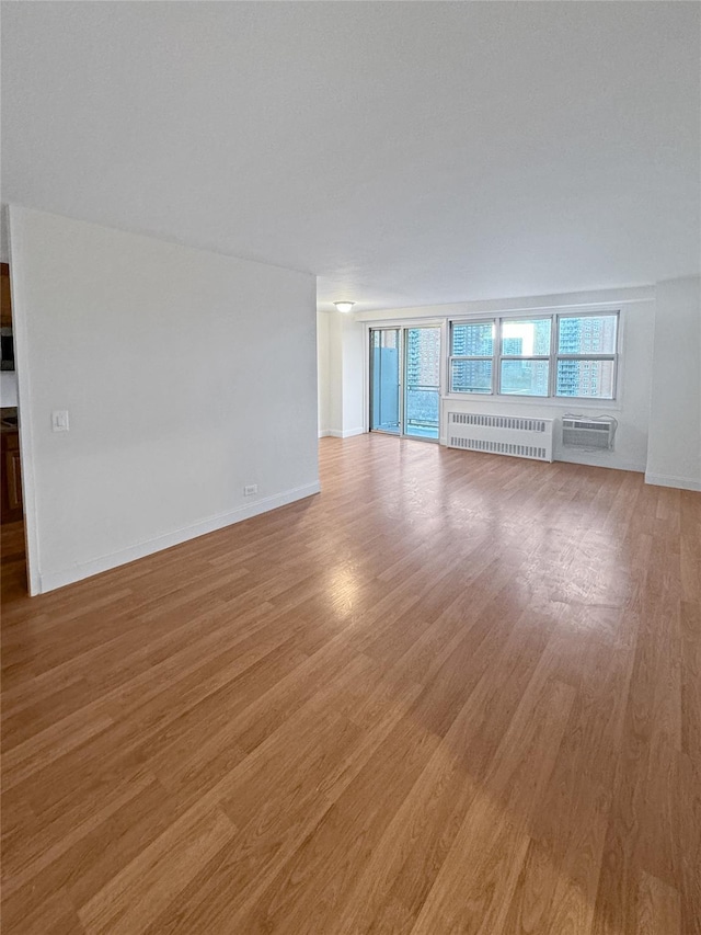 unfurnished room featuring radiator heating unit, a wall unit AC, and light hardwood / wood-style flooring