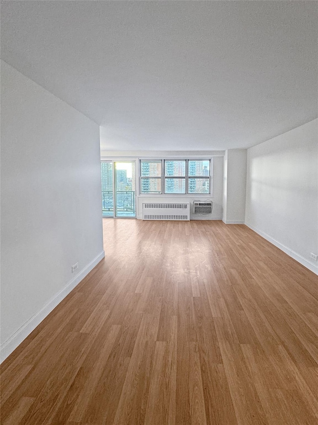 unfurnished living room featuring a textured ceiling, radiator, hardwood / wood-style floors, and a wall mounted air conditioner