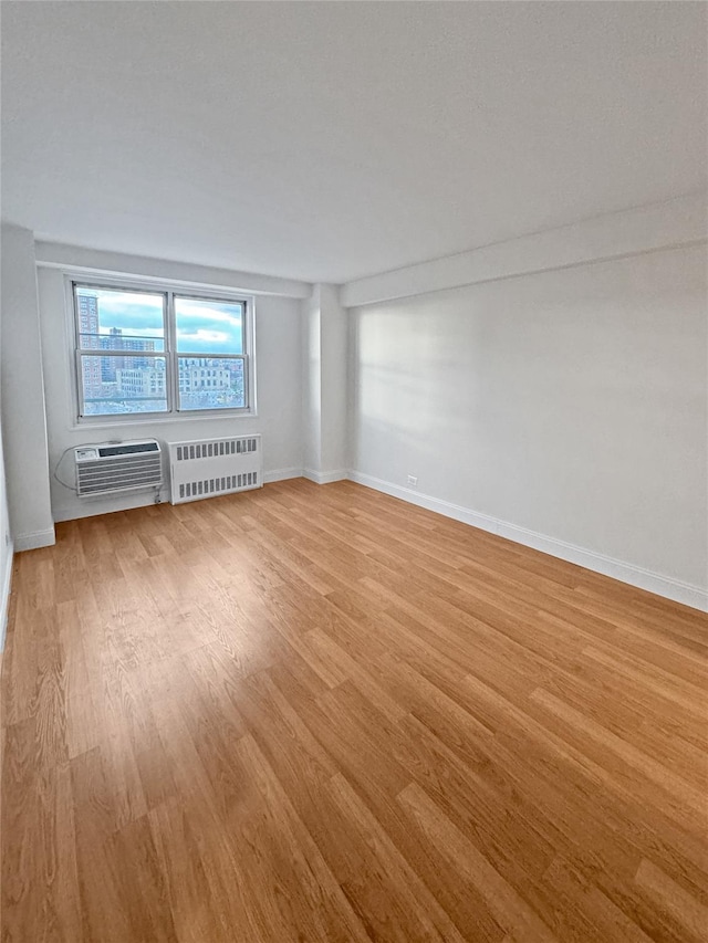 empty room with radiator heating unit, a wall mounted air conditioner, and light hardwood / wood-style flooring