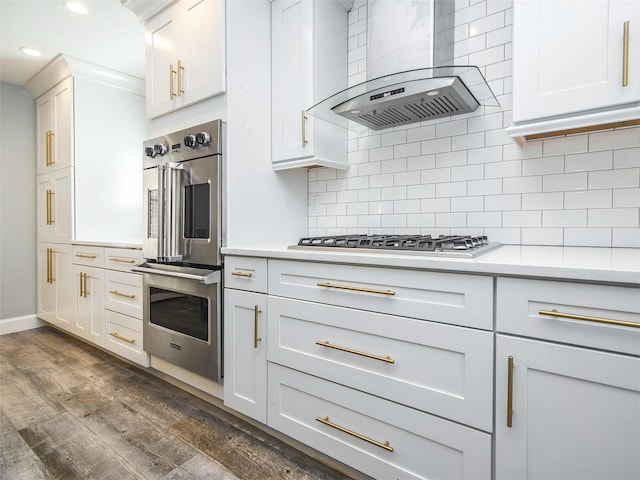 kitchen featuring dark wood-type flooring, white cabinets, wall chimney exhaust hood, appliances with stainless steel finishes, and tasteful backsplash