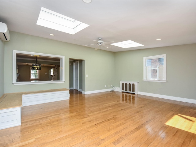 spare room featuring ceiling fan with notable chandelier, light hardwood / wood-style floors, an AC wall unit, and a skylight