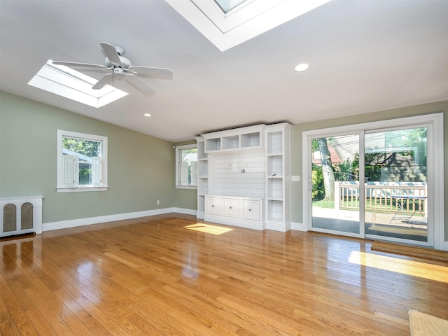 unfurnished living room featuring vaulted ceiling with skylight, ceiling fan, light hardwood / wood-style floors, and a wealth of natural light