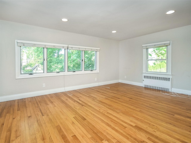 empty room with plenty of natural light, radiator heating unit, and light hardwood / wood-style flooring