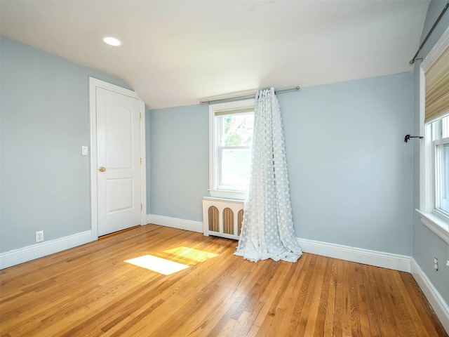 empty room featuring radiator heating unit, vaulted ceiling, and light hardwood / wood-style flooring