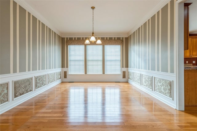 unfurnished dining area with light hardwood / wood-style floors, an inviting chandelier, and ornamental molding