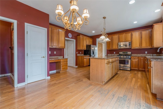 kitchen with light wood-type flooring, appliances with stainless steel finishes, a center island, and decorative light fixtures