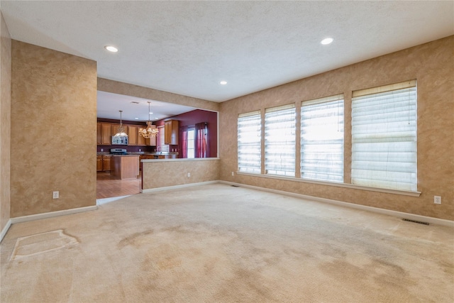 unfurnished living room featuring light carpet, a textured ceiling, and a notable chandelier