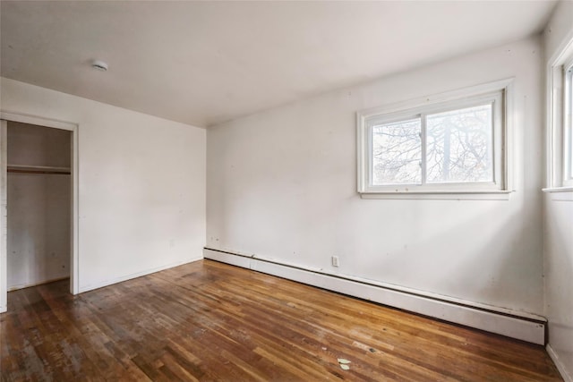 unfurnished bedroom with a closet, dark hardwood / wood-style floors, and baseboard heating