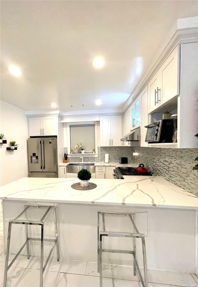 kitchen with stainless steel appliances, white cabinetry, a breakfast bar area, and light stone counters