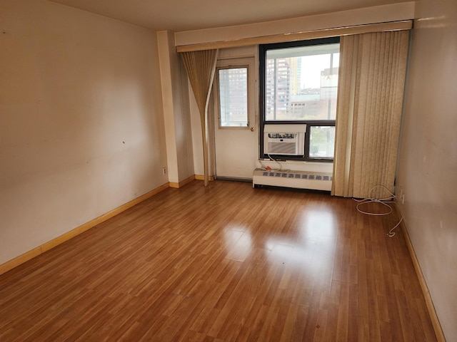 empty room featuring hardwood / wood-style flooring, a baseboard radiator, and cooling unit