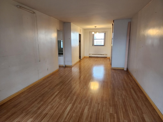 spare room featuring baseboard heating, light hardwood / wood-style floors, and an inviting chandelier