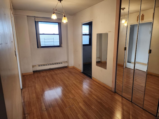 unfurnished bedroom with an inviting chandelier, wood-type flooring, and a baseboard heating unit