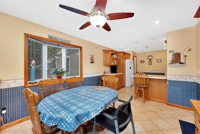 dining room featuring ceiling fan, light tile patterned floors, and tile walls