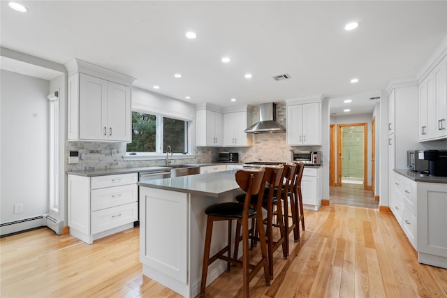 kitchen featuring a center island, white cabinetry, wall chimney range hood, and light hardwood / wood-style floors