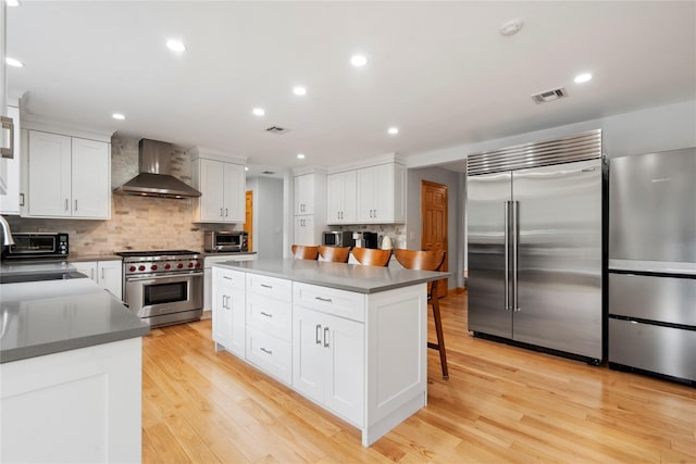 kitchen featuring premium appliances, wall chimney range hood, white cabinets, a kitchen island, and a breakfast bar area