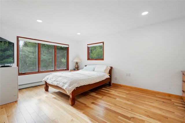 bedroom with light hardwood / wood-style floors and a baseboard heating unit